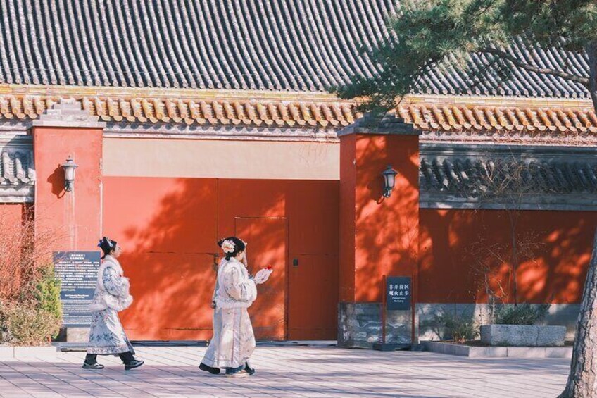 Two people in traditional attire walking past a red building with a tiled roof. 2