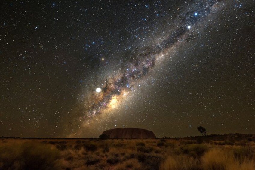 A starry night sky with the Milky Way, a large rock formation, and a person standing in the foreground. 4