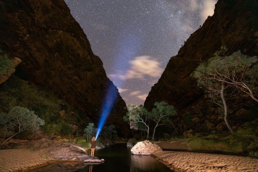 A starry night sky over a canyon with a person standing by a river. 2