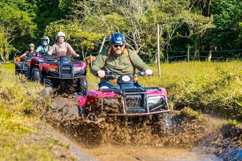 Four people on ATVs navigating a muddy trail in a rural setting. 5