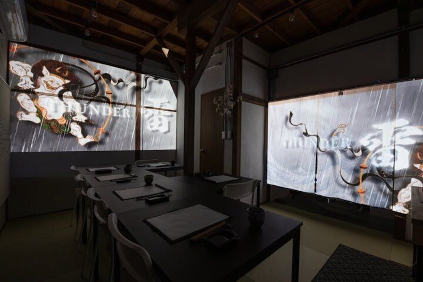 A conference room with a long table, chairs, and a large screen displaying abstract art. 1