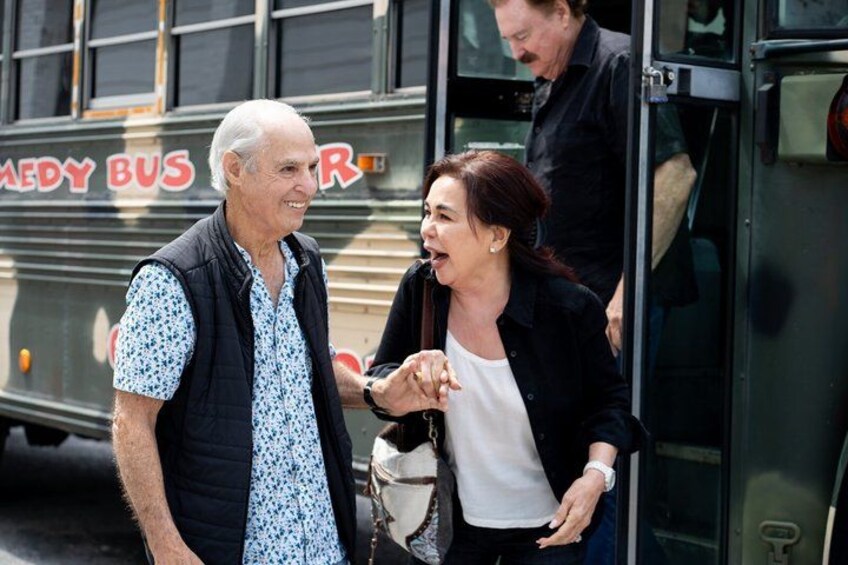 Two people standing in front of a bus with 'COMEDY BUS' written on it. 4