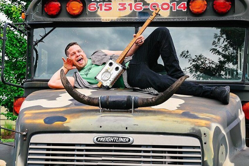 A person lying on the back of a vintage truck with a large horn attached. 3