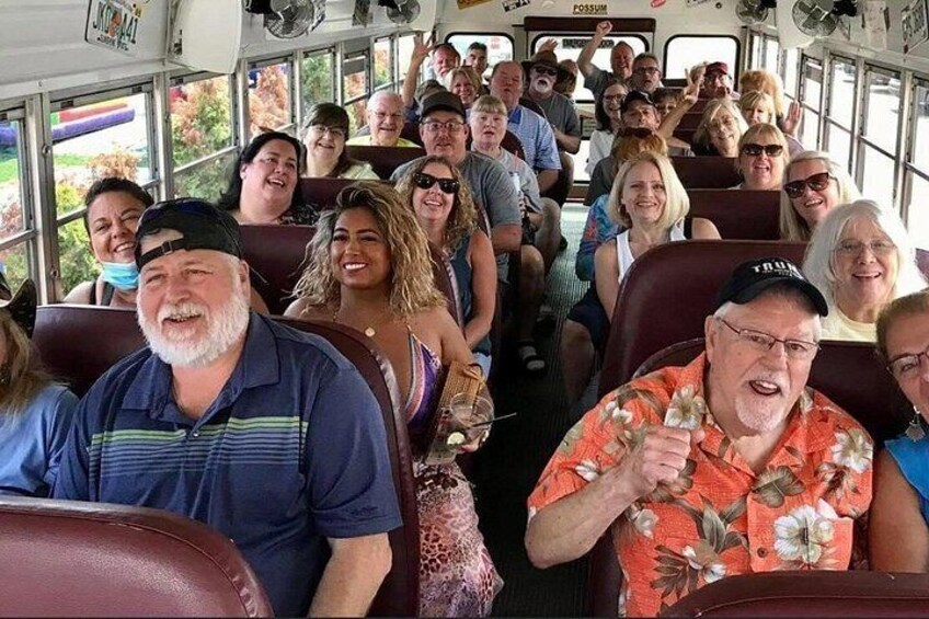 A bus interior with passengers seated and a man in a floral shirt holding a drink. 5