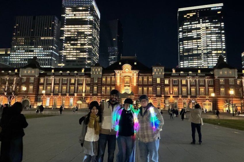 A group of people standing in front of a historic building with illuminated windows and a large central entrance. 4
