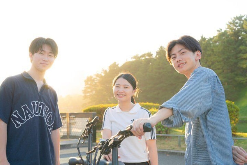 Three people standing outdoors, one holding a bicycle. 1