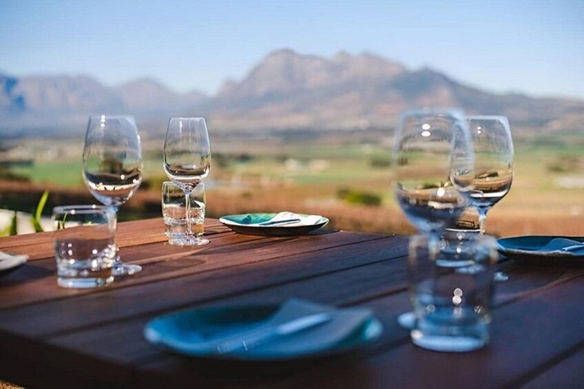 A wooden table with empty wine glasses and plates, set against a mountainous landscape. 1