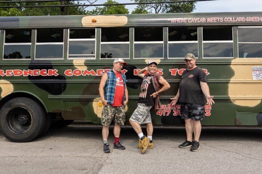 Three people standing in front of a green bus with 'REDNECK COMEDY TOUR' written on it. 1