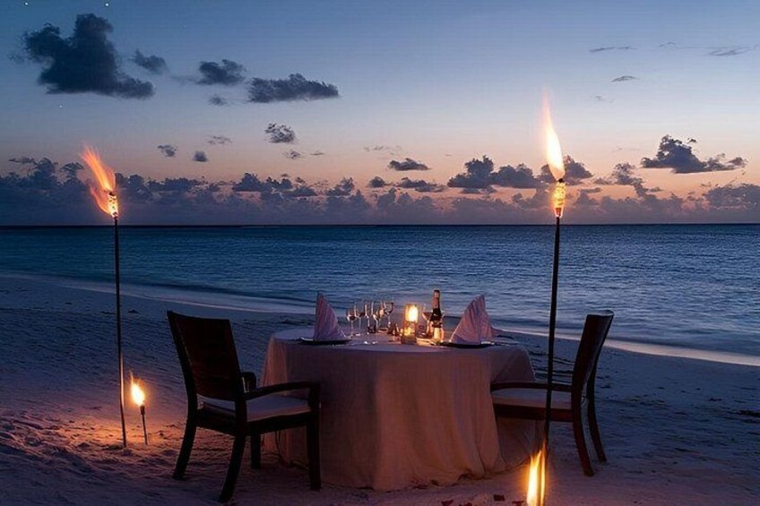 A table set for two on a beach at sunset with torches. 2