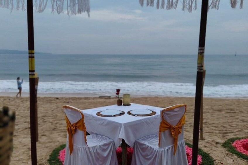 A beach wedding setup with a table and chairs, a person walking in the background, and the ocean. 4