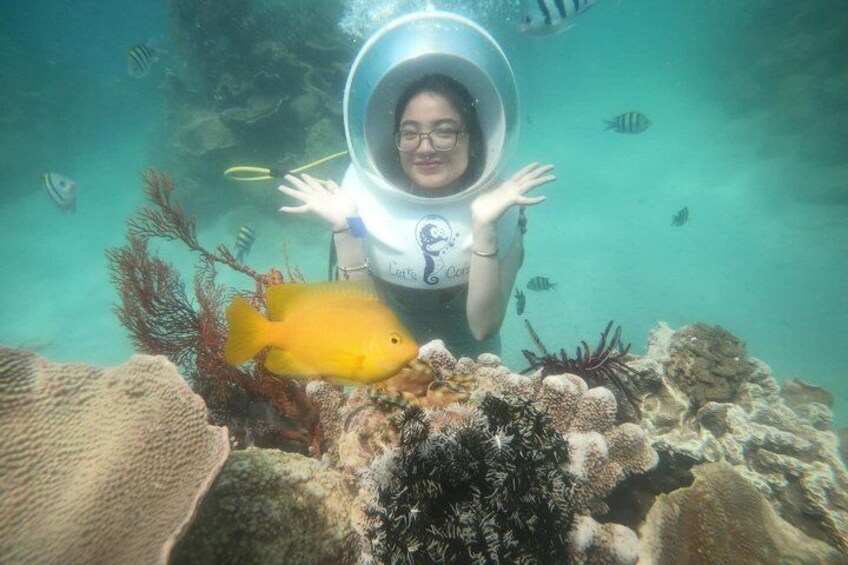 A person in a diving helmet underwater with a yellow fish nearby. 3