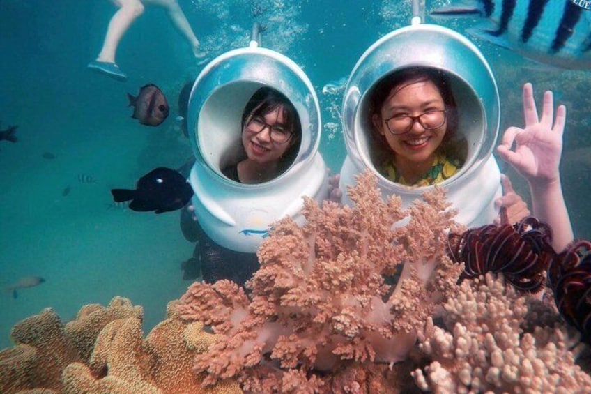 Two people in underwater diving helmets surrounded by coral reefs. 1