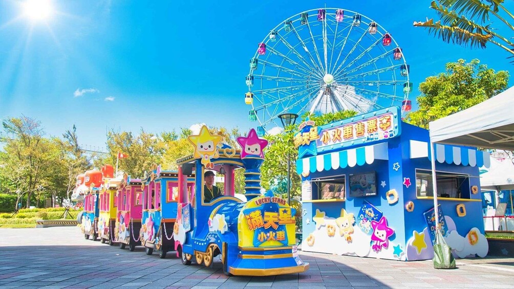 A colorful train with a Ferris wheel and a blue building with stars and a sign. 5