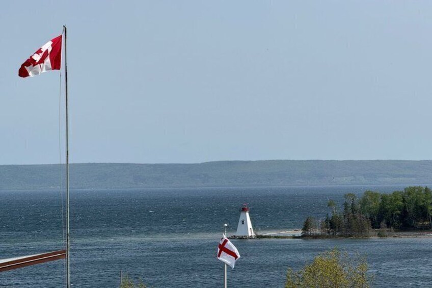 A lighthouse, a Canadian flag, and a British flag by the water. 3