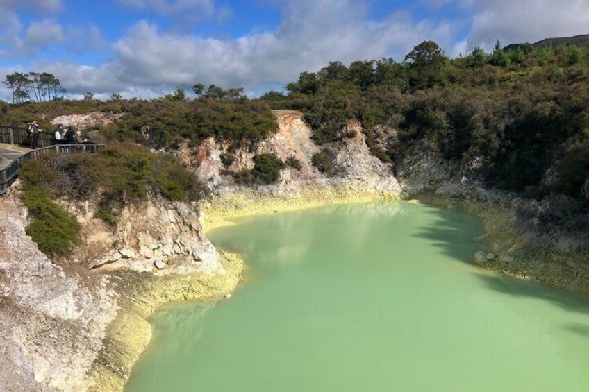 A green mineral pool surrounded by rocky terrain and sparse vegetation. 5