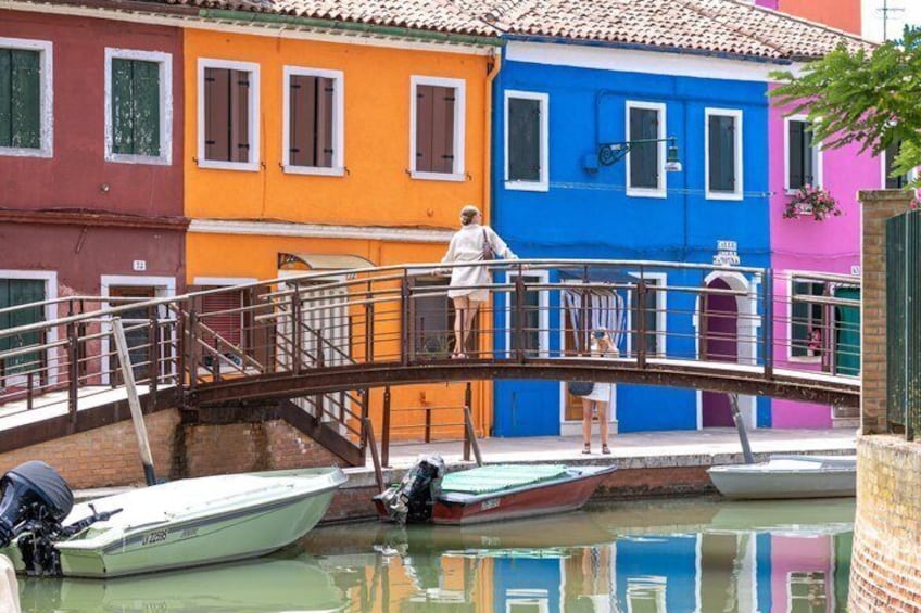 A colorful bridge over a canal with boats, a person on the bridge, and a building with a sign. 5
