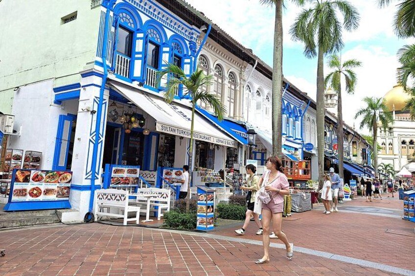 A street with a blue and white building, palm trees, and people walking. 5