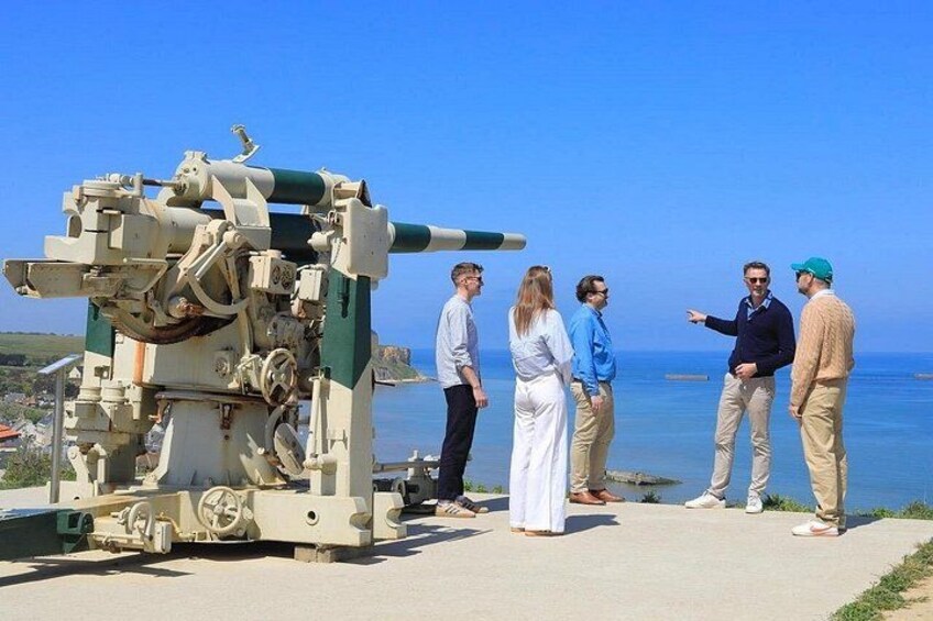 A group of people standing near a large artillery piece on a coastal path. 3