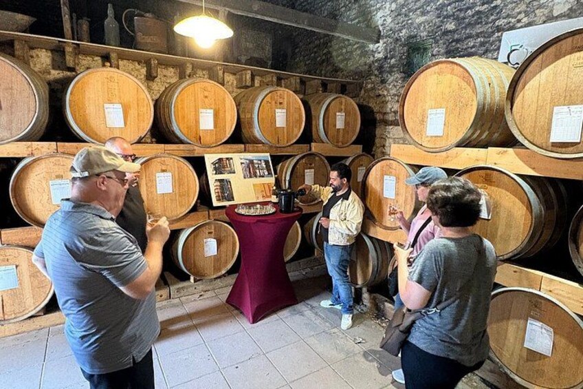 A group of people in a wine cellar with wooden barrels and a table displaying information. 5