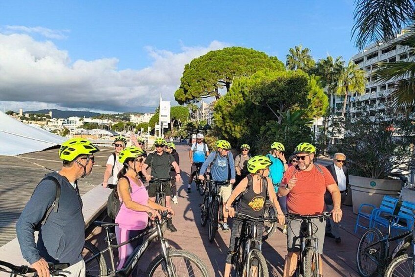 A group of cyclists on a paved path with buildings and trees in the background. 5