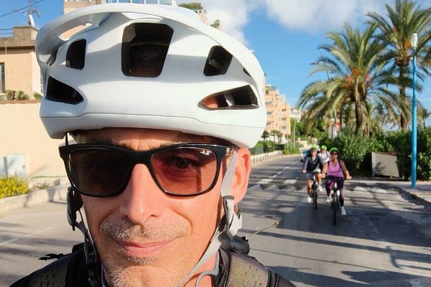 A person wearing a white helmet and sunglasses, with a road and palm trees in the background. 4