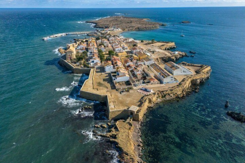 An aerial view of a coastal town with a fortified structure, clear blue waters, and a distant island. 1