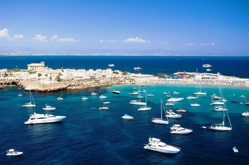 A coastal town with boats anchored in the water, a beach, and a historic building. 3
