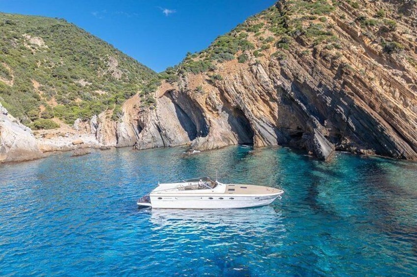 A boat on clear blue water surrounded by rocky cliffs. 3