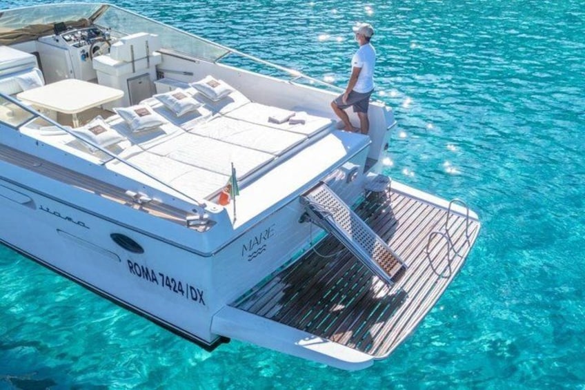 A boat with a person standing on the deck, a name 'ROMA 7424/IX' on the side, and clear blue water. 3