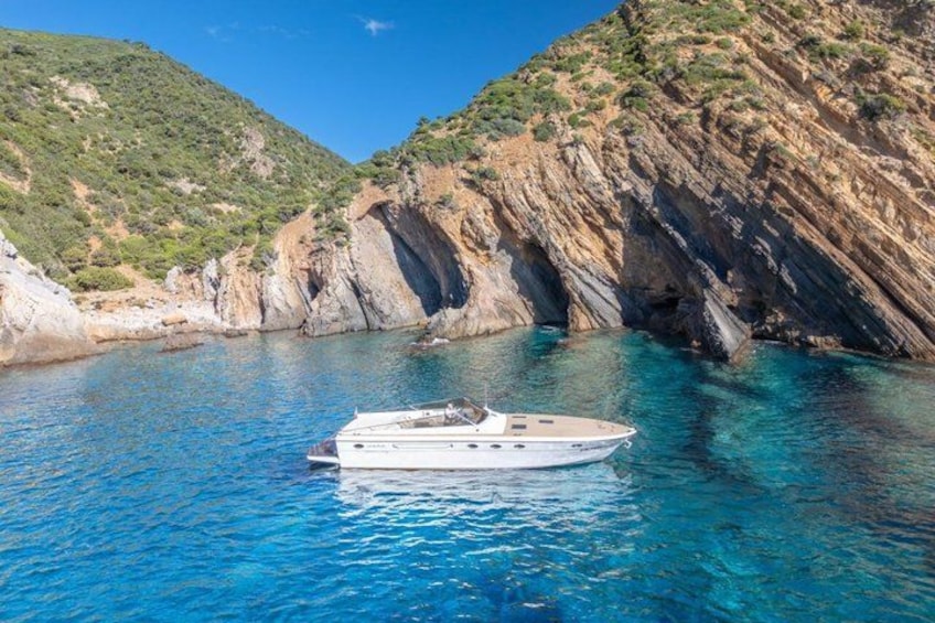 A boat on clear blue water surrounded by rocky cliffs. 2