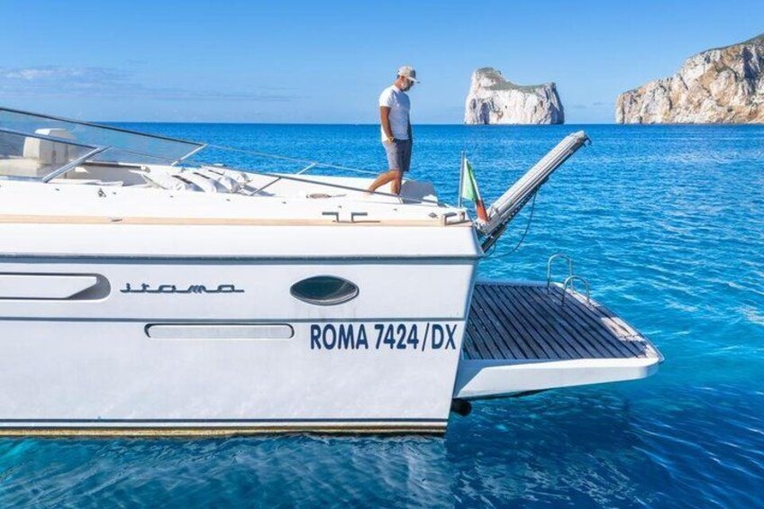 A white boat named 'ROMA 7424/DX' with a person standing on the deck, surrounded by clear blue water and rocky formations in the background. 5