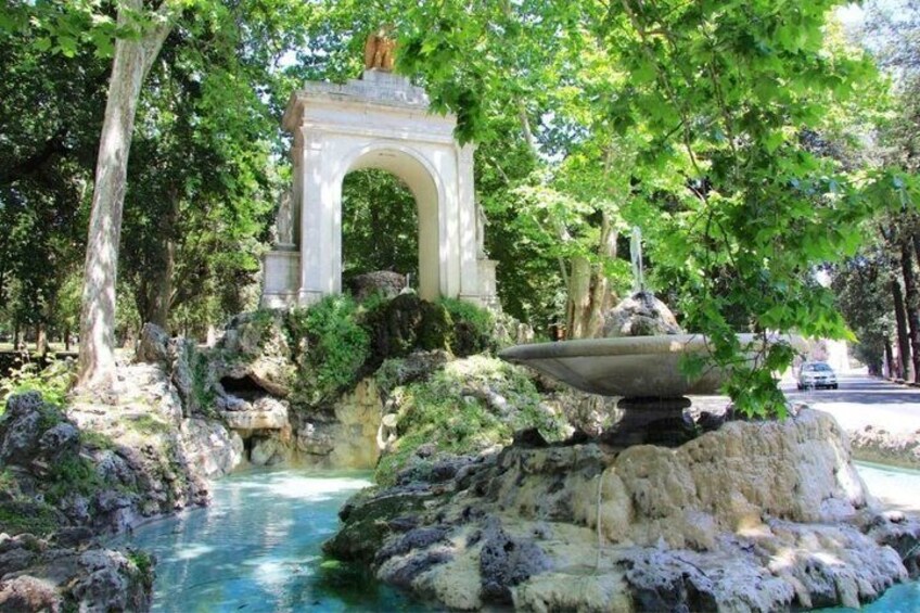 A stone archway, a fountain, and a river in a park. 1