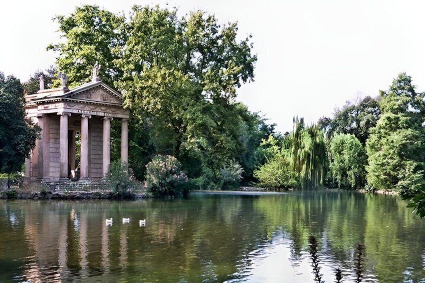 A classical temple with columns, a calm lake, and surrounding trees. 4