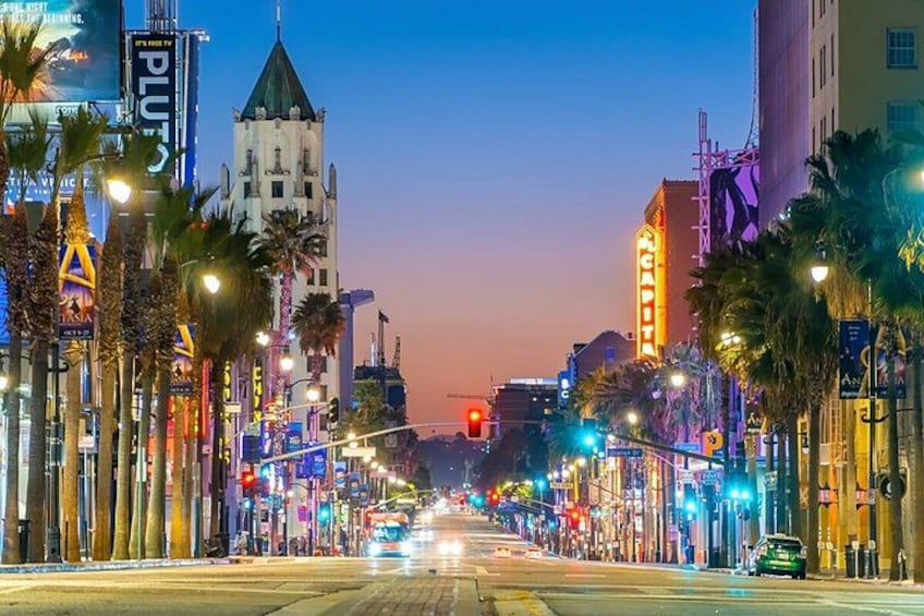 A city street at dusk with illuminated buildings and palm trees. 5