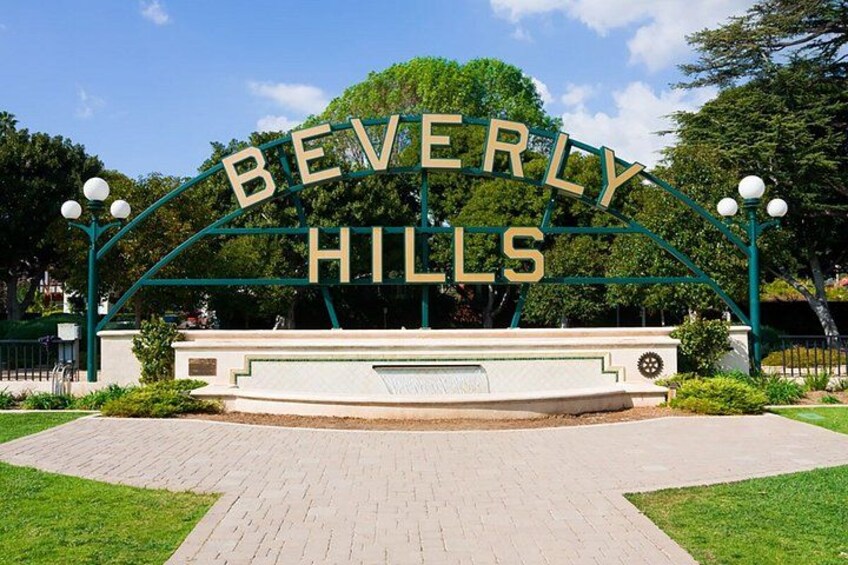 A sign with 'BEVERLY HILLS' written on it, surrounded by a paved area and greenery. 3