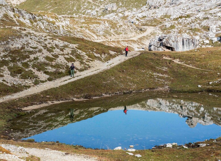 A mountainous landscape with a small lake, hikers on a trail, and rocky terrain. 2