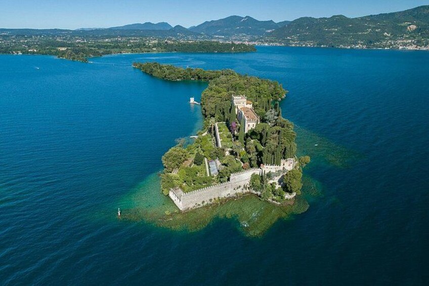An aerial view of a small island with a castle, surrounded by water and mountains in the background. 3