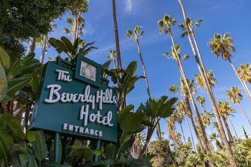 A sign for The Beverly Hills Hotel entrance surrounded by tall palm trees. 4