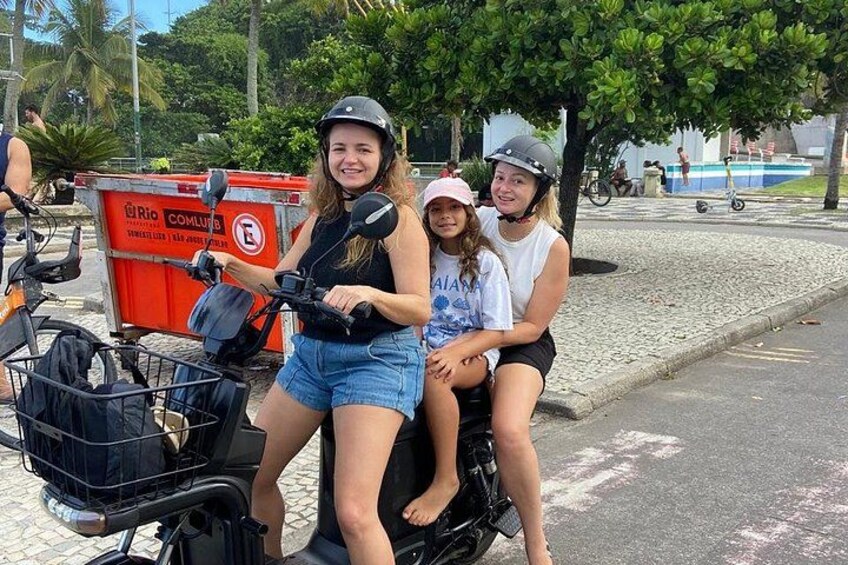 Two people on a scooter, a red trash bin, and a paved street with trees. 3