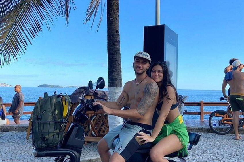 A couple on a scooter with a beach and palm trees in the background. 4