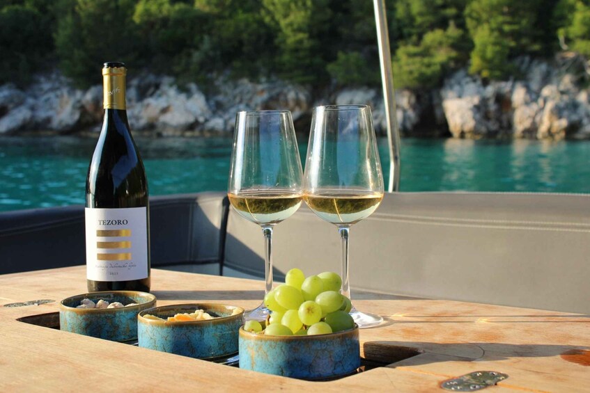 A bottle of Tezoro wine, two glasses with white wine, and a bowl of green grapes on a boat. 1