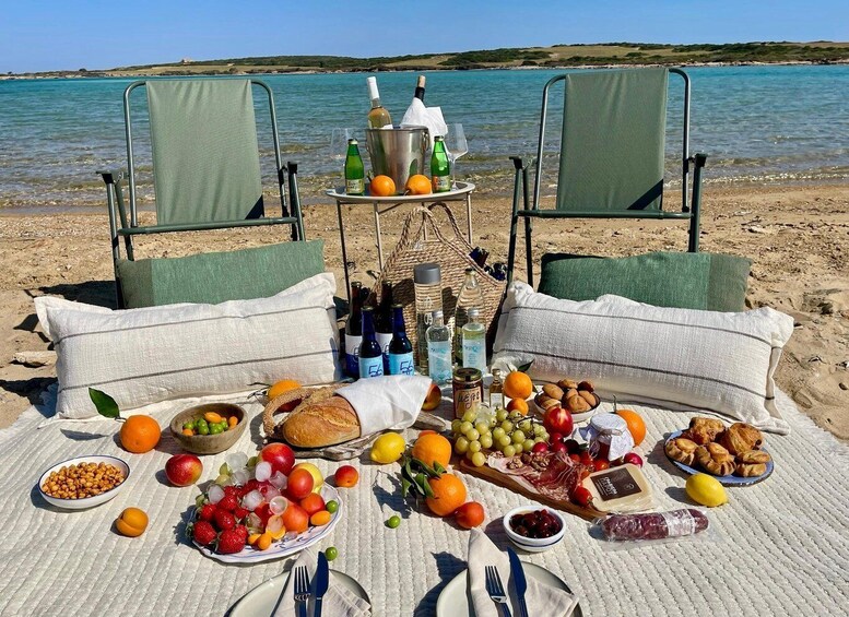 A picnic setup on a beach with chairs, a table with food and drinks, and a view of the sea. 1