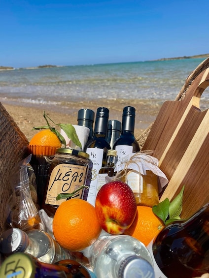 A picnic basket on a beach with bottles, oranges, and an apple. 3
