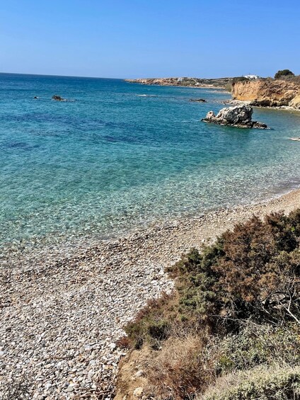 A rocky beach with clear blue water and distant cliffs. 4