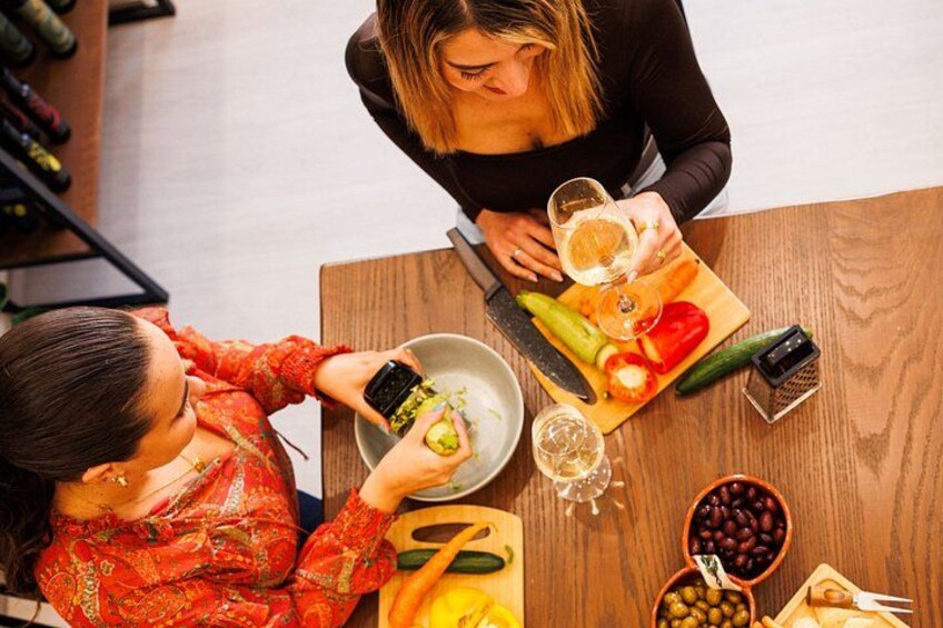 Two people sitting at a wooden table with food and drinks, including a bowl of olives and a glass of wine. 3