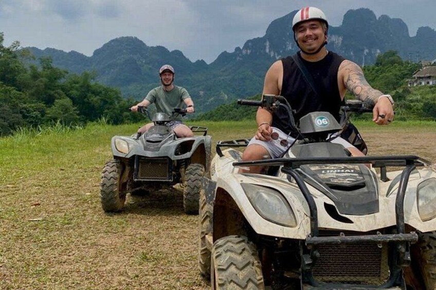 Two people on ATVs on a grassy field with mountains in the background. 1