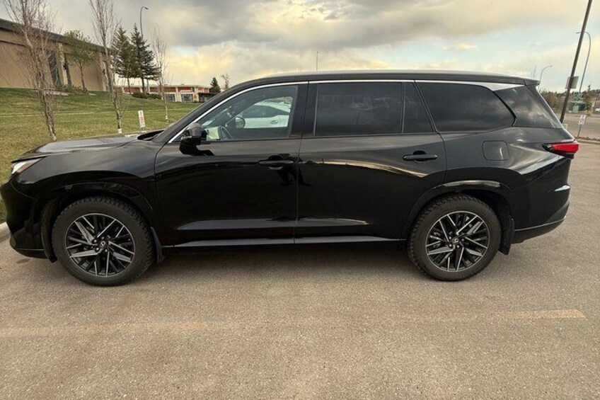 A black SUV parked on a paved surface with a grassy area and a building in the background. 5