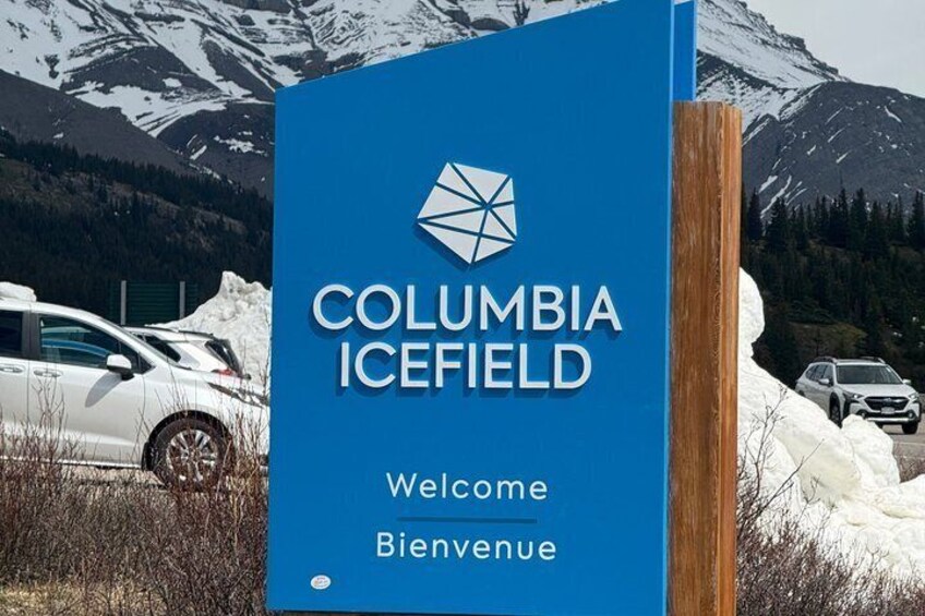 A blue sign with 'COLUMBIA ICEFIELD Welcome' and a mountain landscape in the background. 1