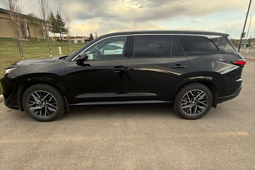 A black SUV parked on a paved surface with a grassy area and trees in the background. 3