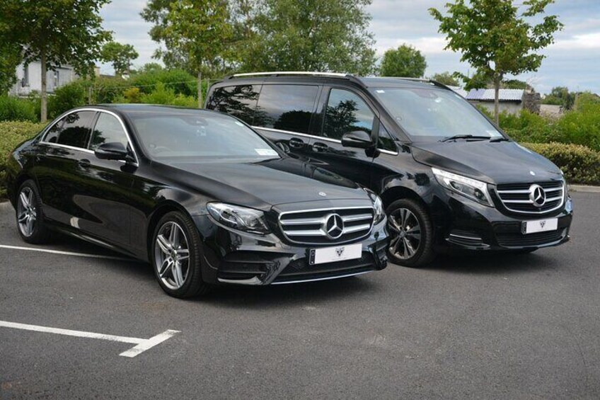 Two black Mercedes-Benz cars parked in a lot with trees and a building in the background. 2